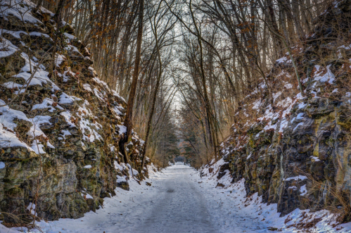 A snowy path flanked by rocky cliffs and bare trees, creating a serene winter landscape.