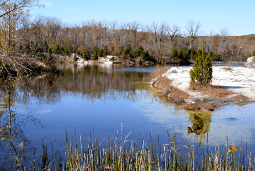 A serene pond surrounded by trees and rocky shores, reflecting the clear blue sky and autumn foliage.