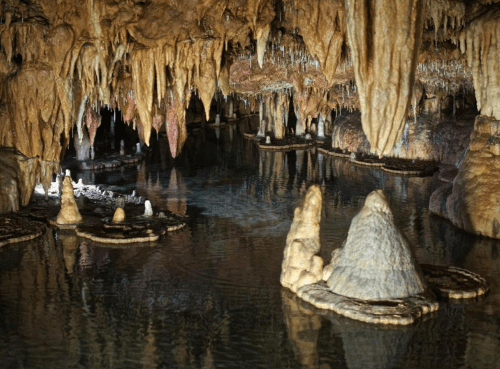 A serene underground cave with stalactites and stalagmites reflected in still water.