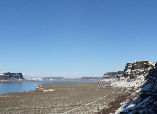 A scenic view of a snowy landscape with cliffs, a river, and a clear blue sky.