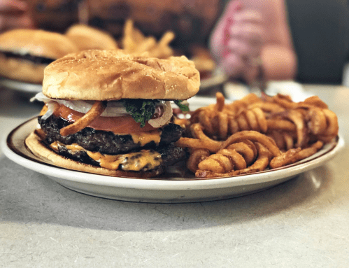 A juicy cheeseburger with lettuce, tomato, and onion, served with curly fries on a plate.
