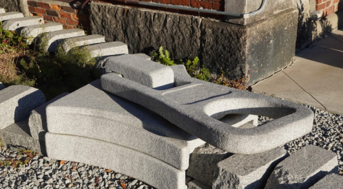 A collection of large, irregularly shaped granite stones arranged on gravel near a brick wall.