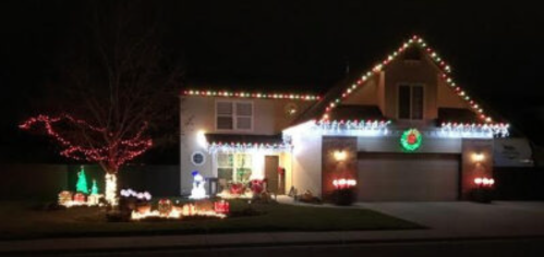 A house decorated with colorful Christmas lights, featuring a snowman and festive lawn decorations at night.