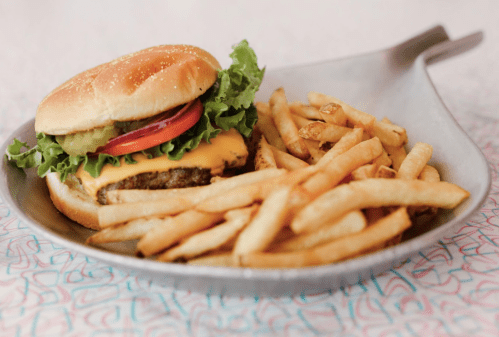 A cheeseburger with lettuce, tomato, and pickles served with a side of golden French fries on a plate.