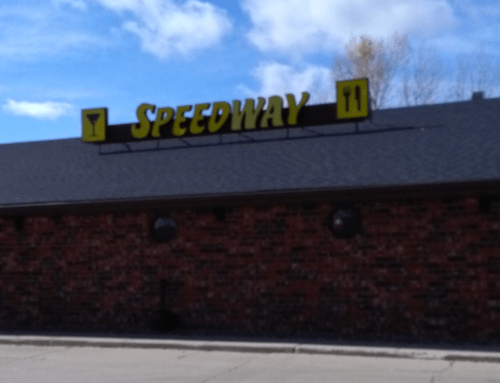 Sign on a building reads "SPEEDWAY" in large yellow letters against a blue sky and brick wall.
