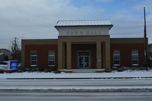 A snow-covered town hall building with a sign out front, featuring a modern design and large entrance.