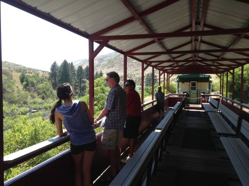 Four people stand on a covered deck overlooking a lush green landscape and river, enjoying the scenic view.