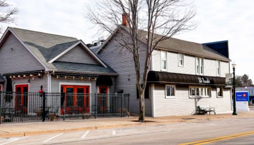 A two-story building with a gray exterior, featuring red doors and a black awning, located on a street.