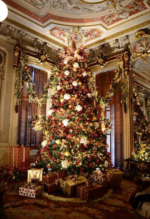 A beautifully decorated Christmas tree with red and gold ornaments, surrounded by wrapped gifts in an elegant room.