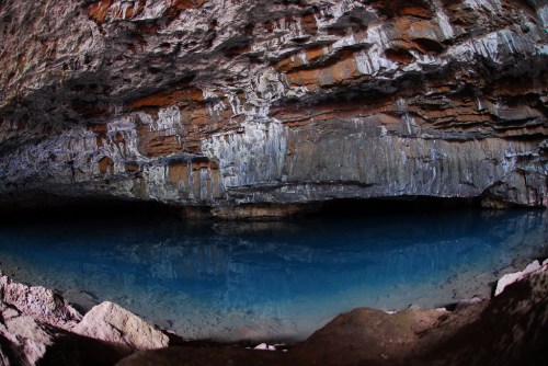 A serene underground cave with colorful rock formations and a clear blue pool of water reflecting the surroundings.