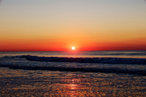 A serene sunset over the ocean, with vibrant orange and yellow hues reflecting on the water's surface.