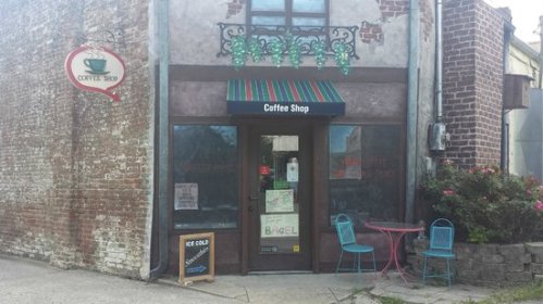 A quaint coffee shop with a colorful awning, outdoor seating, and a rustic brick facade.