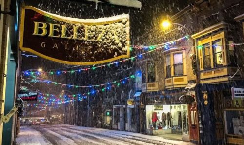 A snowy street scene with colorful lights and a sign for "Belleza Gallery" in a quaint town.