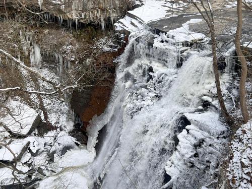A frozen waterfall surrounded by icy rocks and bare trees, with icicles hanging from the cliffs above.