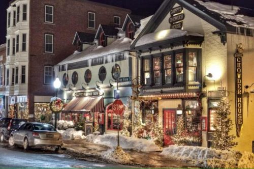 Charming snowy street scene at night, featuring festive restaurants and holiday decorations.
