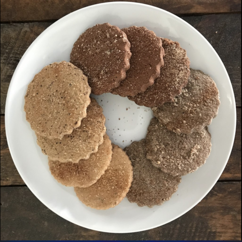 A white plate with an assortment of round cookies in various shades of brown, arranged in a circular pattern.