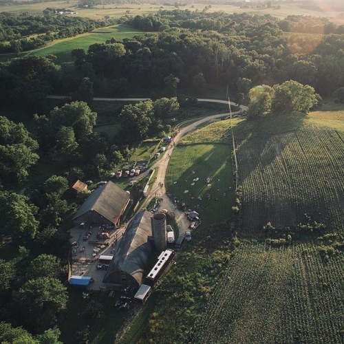 Aerial view of a rural farm with a barn, fields, and winding road surrounded by lush greenery.