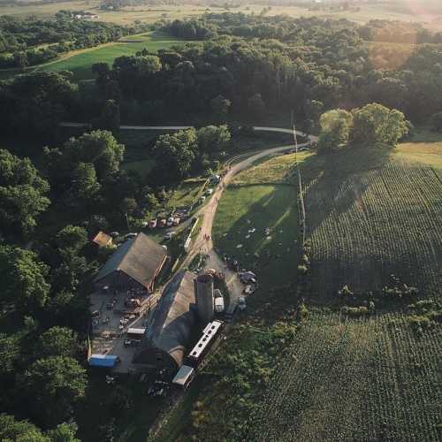 Aerial view of a rural farm with a barn, fields, and winding road surrounded by lush greenery.