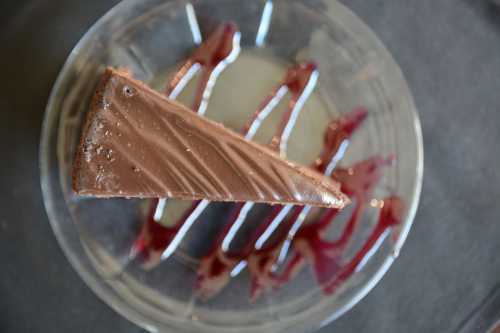 A slice of chocolate cake on a plate, drizzled with berry sauce.