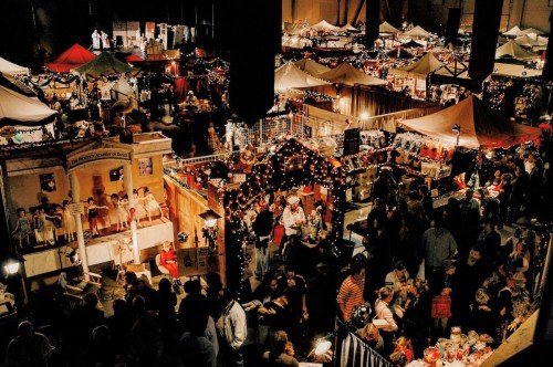 A bustling holiday market filled with festive stalls, lights, and crowds of people enjoying the seasonal atmosphere.