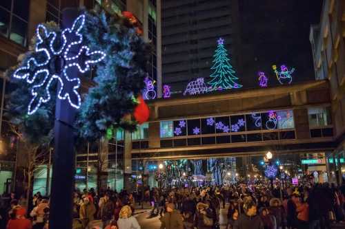 A festive street scene with holiday lights, decorations, and a crowd enjoying the winter atmosphere at night.