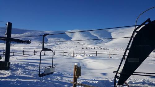A snowy landscape with ski lift chairs and distant hills under a clear blue sky.