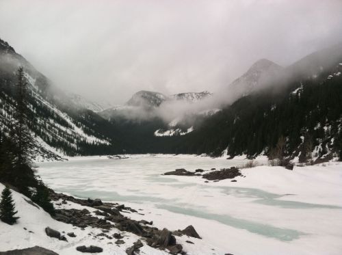A serene, snowy landscape with a frozen lake surrounded by mountains and misty clouds.