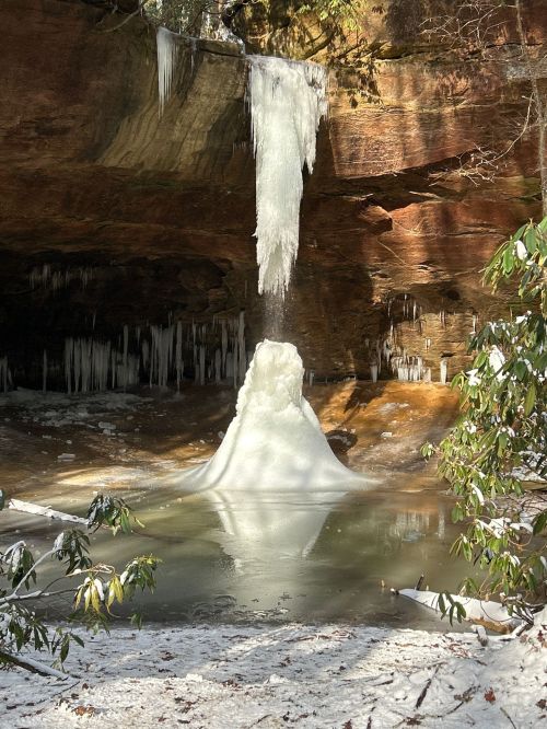 A frozen waterfall cascades into a serene pool, surrounded by icy formations and snow-covered rocks.