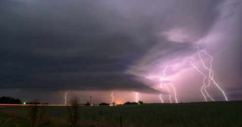 A dramatic sky filled with dark clouds and multiple lightning strikes illuminating the landscape at dusk.