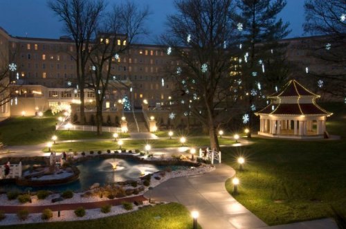 A serene night scene featuring a gazebo, pond, and snowflake lights in a landscaped area.
