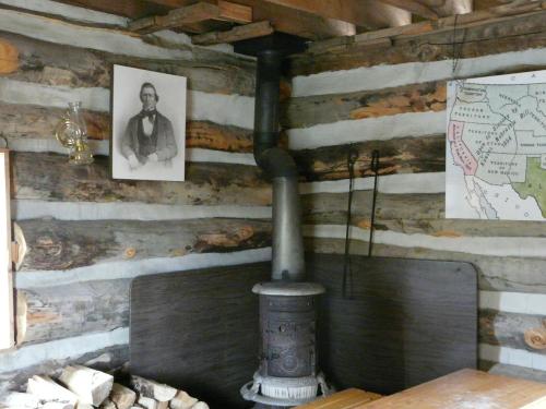 Interior of a rustic cabin featuring a wood stove, a portrait on the wall, and a map of the United States.