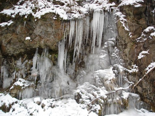 Icicles hanging from a rocky surface, surrounded by snow and ice, creating a wintery landscape.