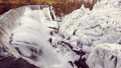 A frozen waterfall cascading over rocks, surrounded by icy formations and winter scenery.