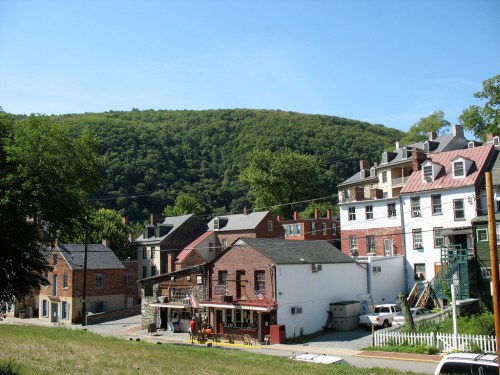 A scenic view of a small town with historic buildings and a lush green hillside in the background under a clear blue sky.