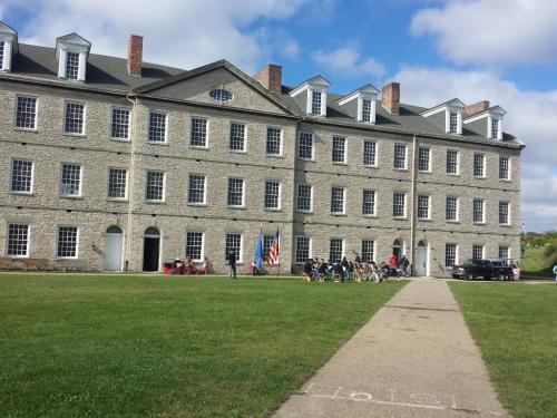 Historic stone building with people gathered outside on a grassy area, under a partly cloudy sky.