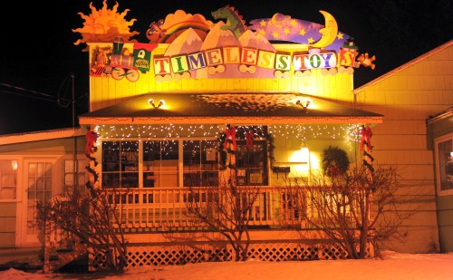Colorful storefront of "Timeless Toys" decorated with lights and playful designs, set against a snowy backdrop.