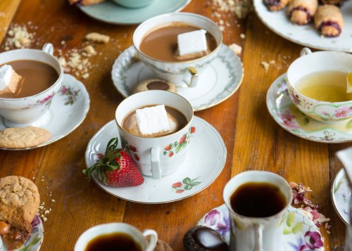 A cozy tea setting with various cups of tea and coffee, cookies, and a strawberry on a wooden table.