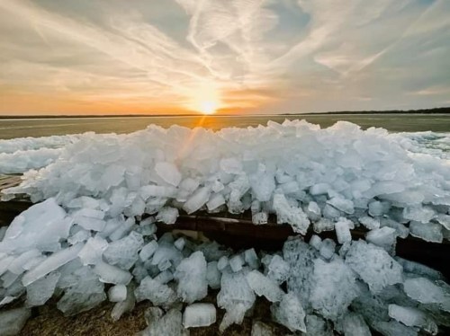 A sunset over a frozen landscape, with large chunks of ice piled up in the foreground.