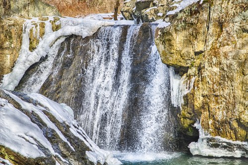 A frozen waterfall cascading over rocky cliffs, surrounded by ice and winter scenery.
