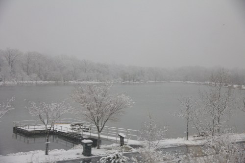 A snowy landscape featuring a frozen lake, bare trees, and a small dock surrounded by a wintery scene.