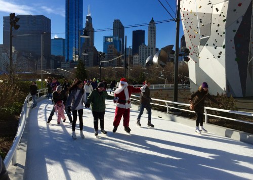 A festive scene of people ice skating, including someone in a Santa costume, with a city skyline in the background.