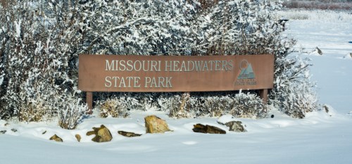 Sign for Missouri Headwaters State Park surrounded by snow and rocks in a winter landscape.