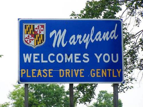 Blue welcome sign for Maryland featuring the state flag and the message "Please Drive Gently."