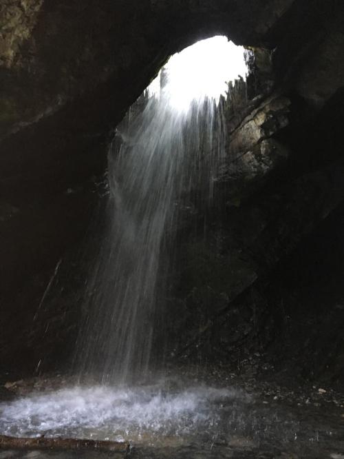 Water cascades down from a rocky opening, creating a serene waterfall effect in a dark cave.