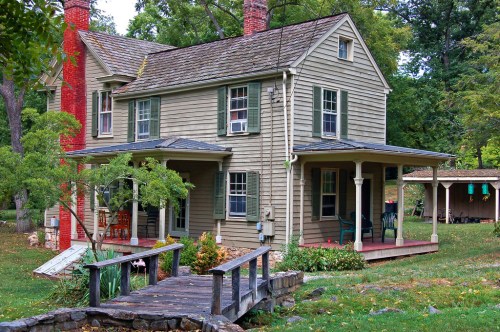 A charming two-story house with a porch, surrounded by greenery and a small pond in the front yard.
