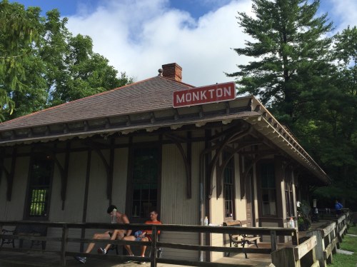 Historic train station in Monkton, surrounded by trees, with a sign displaying the town's name.