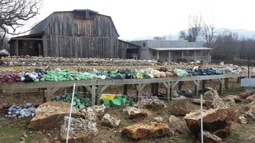 A rustic barn with a display of colorful rocks and minerals in front, set in a rural landscape.