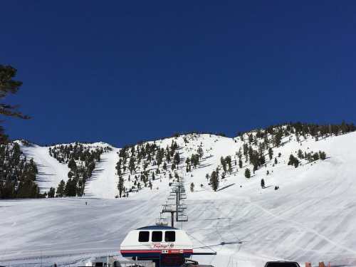 A ski lift stands in front of snow-covered mountains under a clear blue sky.