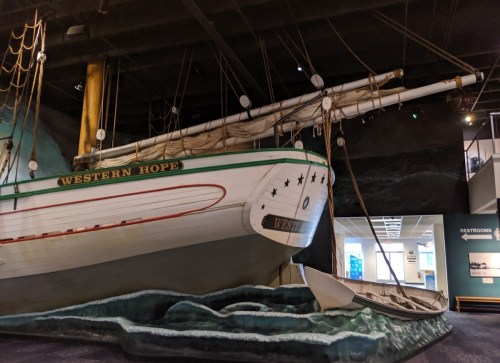 A large ship model named "Western Hope" displayed in a museum, with a small boat alongside it.