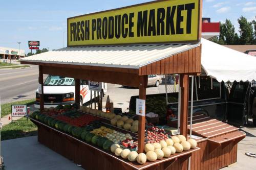A colorful fruit and vegetable stand with a sign reading "Fresh Produce Market" on a sunny day.